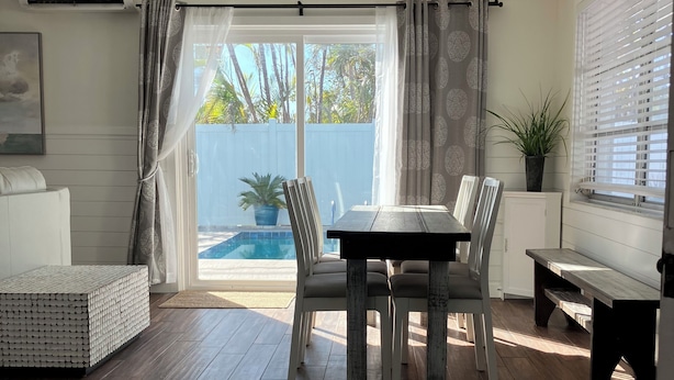 A dining area with a table and chairs, a ceiling fan, a window with blinds, and a view of a swimming pool. - Anna Maria 2 Family Home w/ pool, beach/3 blocks. (Holmes Beach)