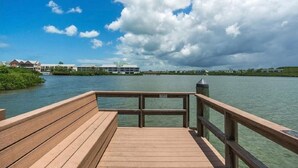Une jetée en bois offrant une vue sur une étendue d’eau calme et sur des bâtiments en arrière-plan.