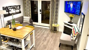 A modern living room with a wooden dining table, a sofa, a television, and a sliding glass door leading to a balcony. - New Basement Private Suite - Fully Furnished,  1 BEDROOM & Futon (Vancouver)