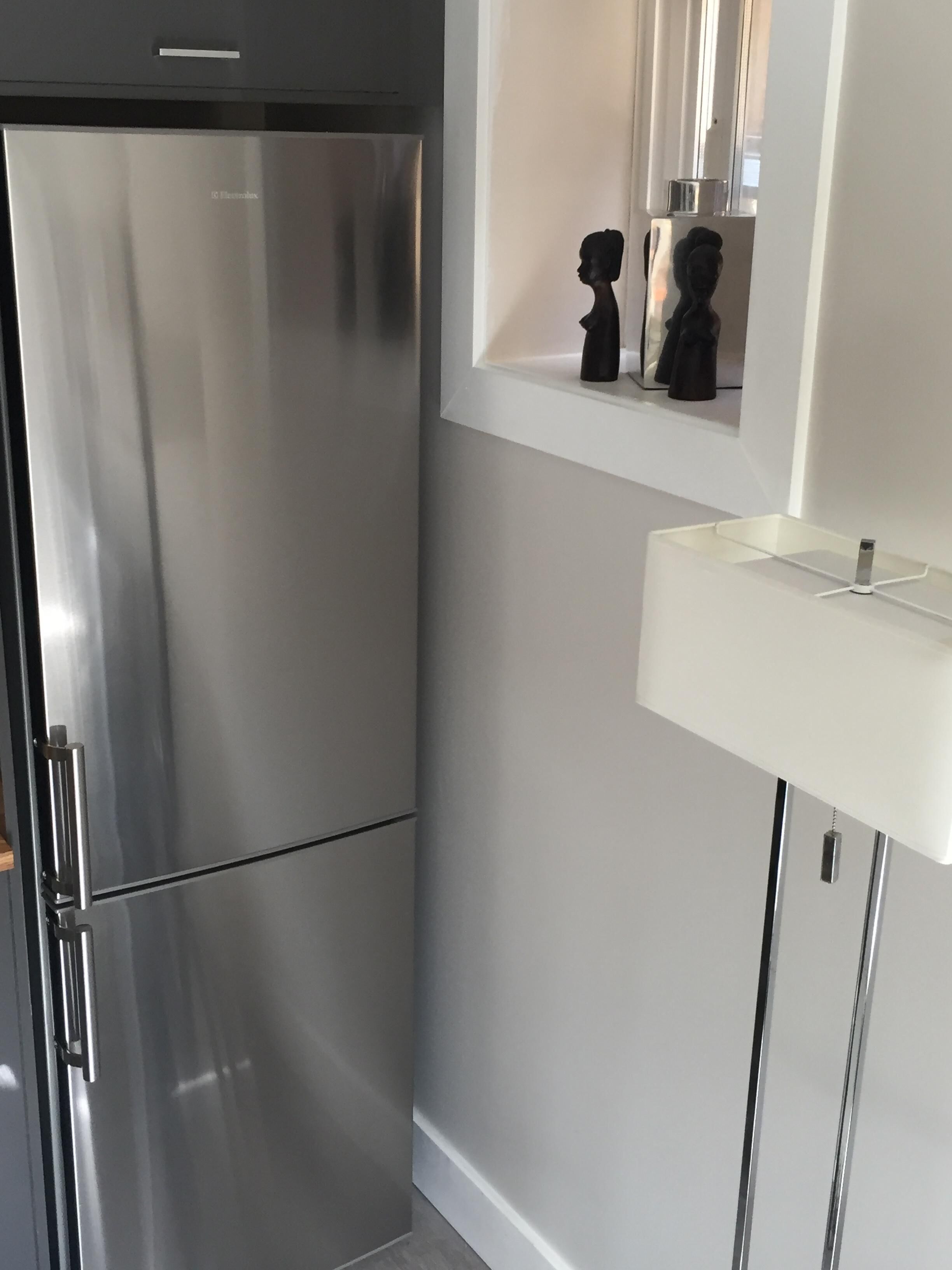 A modern kitchen with a stainless steel refrigerator, a white countertop, and a small shelf with decorative items.