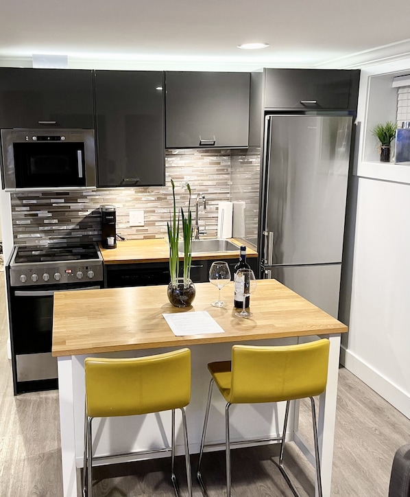 A modern kitchen with a central island, stainless steel appliances, and yellow chairs.