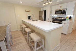 A modern kitchen with a central island, bar stools, a built-in oven, microwave, and a refrigerator.