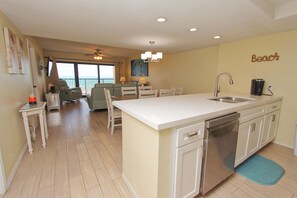 A modern kitchen with a central island, a dining area with chairs, and a view to the outside.