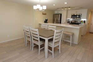 A modern kitchen with a central island, white cabinetry, and a dining area with a wooden table and chairs. - Experience the ocean views at Dreams of Atlantis - Condo 502, a 2BR retreat in South Padre Island. (South Padre Island)