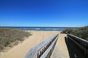 Ein hölzerner Steg führt zu einem Sandstrand, im Hintergrund das Meer.