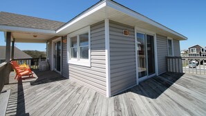 A small, single-story building with a covered deck area, featuring a sliding glass door and a small porch with two orange chairs. - 4 Bedroom, 2.5 bath, sleeps 10, 1 block to beach with beach access and Hot Tub! (Nags Head)