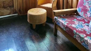 Ein Holzhütten-Interieur mit einem Korbsessel, einem Hocker und einem Sofa mit Blumenmuster.