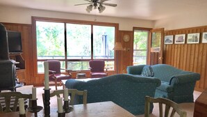 Ein gemütliches Wohnzimmer mit Holztisch, blauem Sofa und einem großen Fenster mit Blick auf Grünflächen.