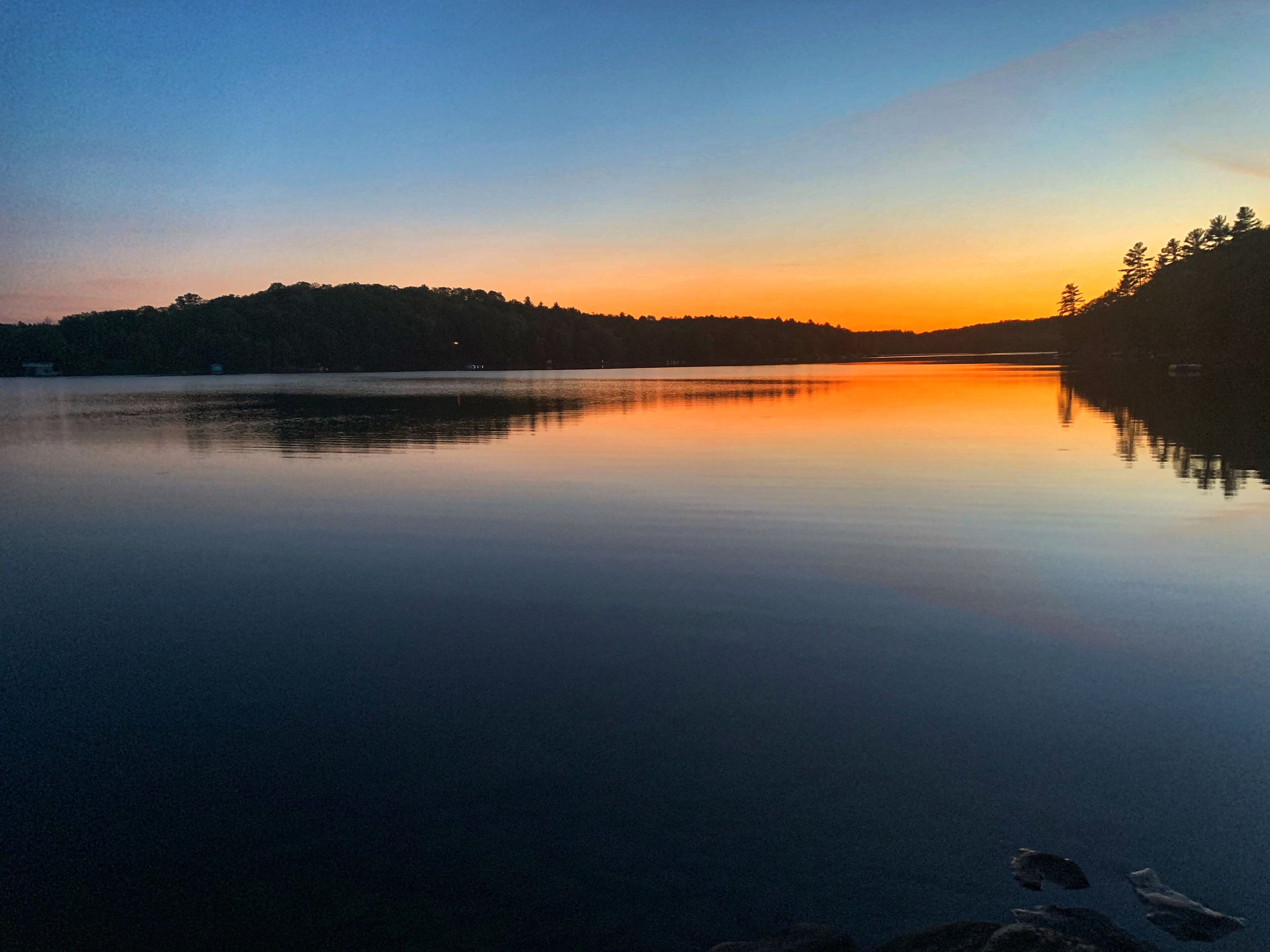 Un lac paisible au coucher du soleil, avec une colline boisée en arrière-plan.