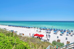 Ein Strand mit weißem Sand, blauen Sonnenschirmen und klarem türkisblauem Wasser.
