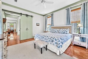 Ein Schlafzimmer mit Bett, Nachttisch, Lampe, einer Bank, einem Kleiderschrank und einer Tür.
