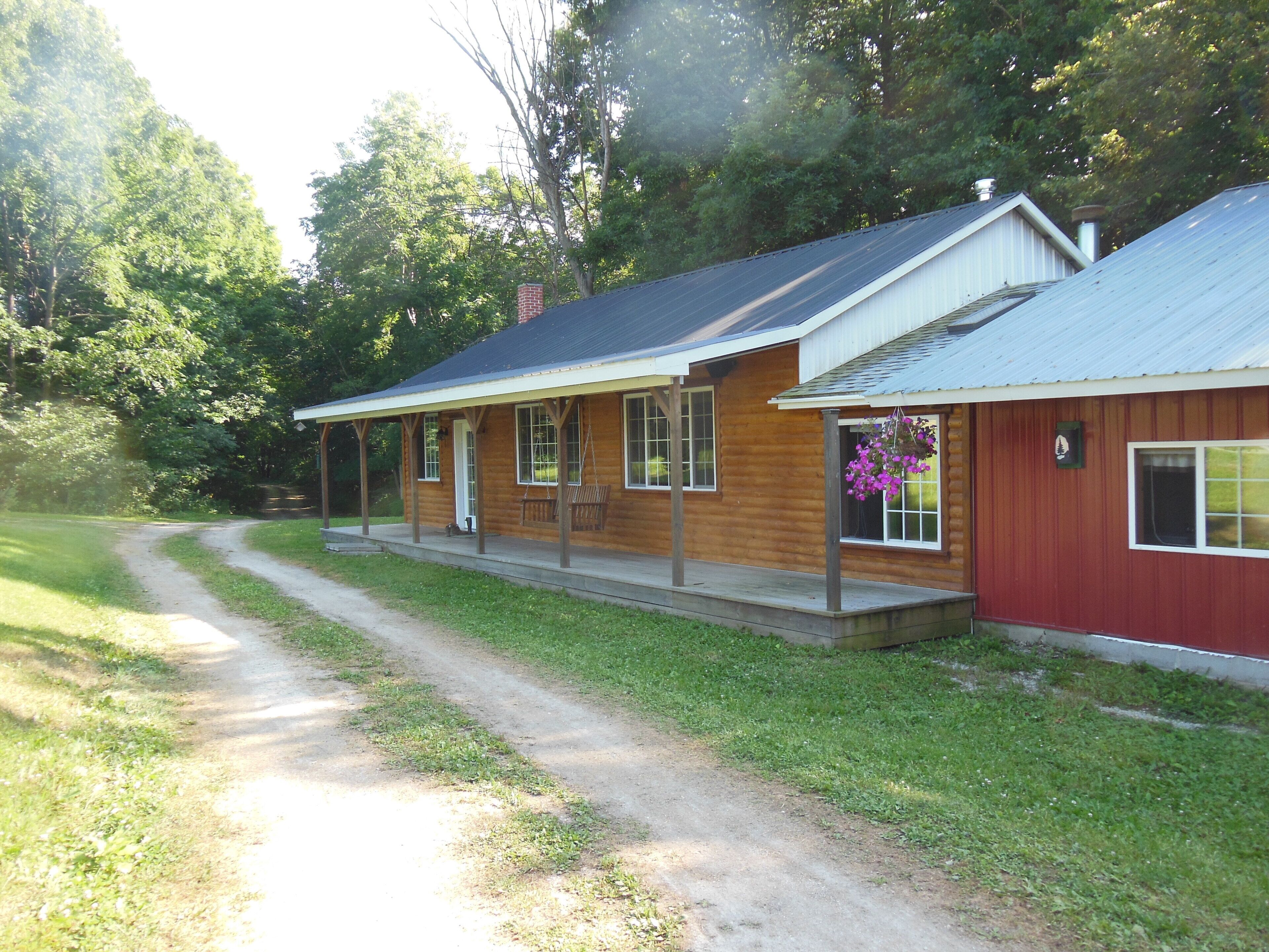 A log cabin with a porch, a covered walkway, and a red exterior.