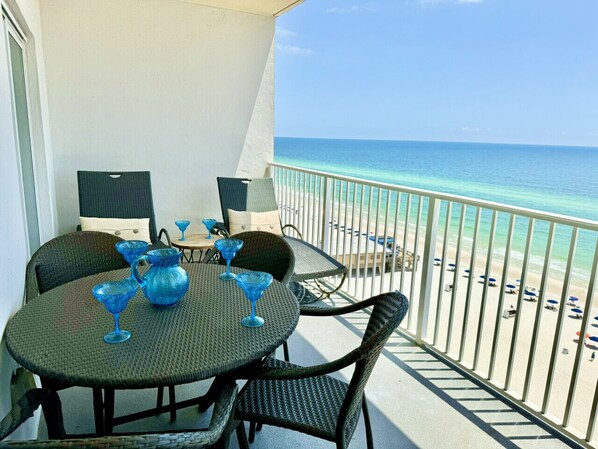 A balcony with a table and chairs, a view of the beach, and a railing.