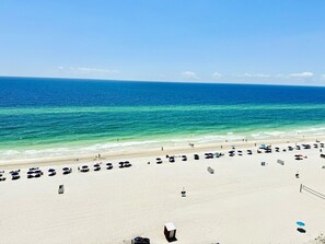 A beach with umbrellas and beach chairs, a volleyball net, and a clear blue sky.