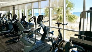 Ein Fitnessstudio mit Cardiogeräten und großen Fenstern mit Blick auf einen Strand.