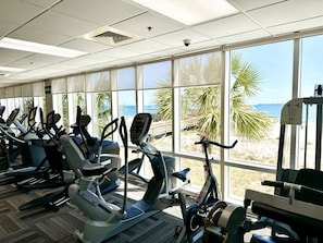 A gym with cardio machines and large windows overlooking a beach.