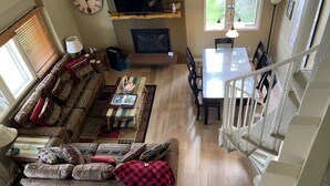 A spacious living area with a sofa set, a dining table, and a TV mounted on a wooden shelf.