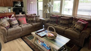 A cozy living room with a sectional sofa, a coffee table, and a kitchen area in the background.