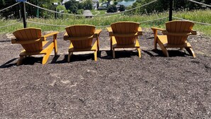 Four Adirondack chairs facing a scenic view of a town and landscape.