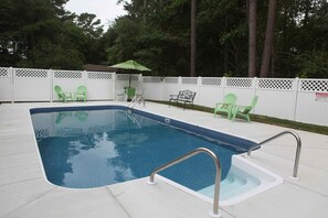 Une piscine rectangulaire avec un escalier en métal, entourée d’une clôture blanche agrémentée de panneaux en treillis.