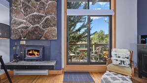 A modern living room with a stone fireplace, wooden flooring, and a glass door leading to an outdoor deck. - ✨ Ski-In/Out Mountain Complex ⎮WIFI + Fireplace + Clubhouse (Steamboat Springs)