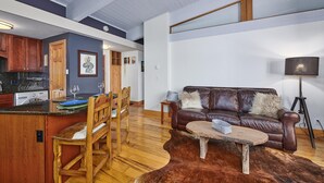 A spacious living area with a leather sofa, wooden coffee table, and a dining area with wooden chairs and a kitchen in the background. - ✨ Ski-In/Out Mountain Complex ⎮WIFI + Fireplace + Clubhouse (Steamboat Springs)