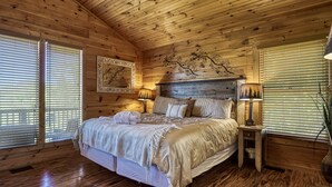 Een gezellig slaapkamer in een houten blokhut, met een groot bed, twee nachtkastjes en een hoofdbord met een decoratieve takkenprint.