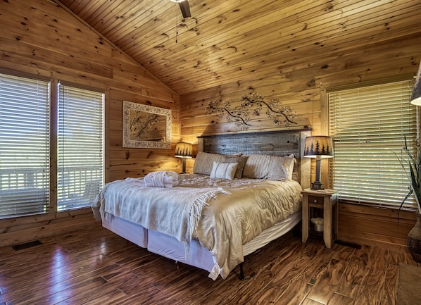 A cozy wooden cabin bedroom with a large bed, two bedside tables, and a headboard with a decorative branch design.