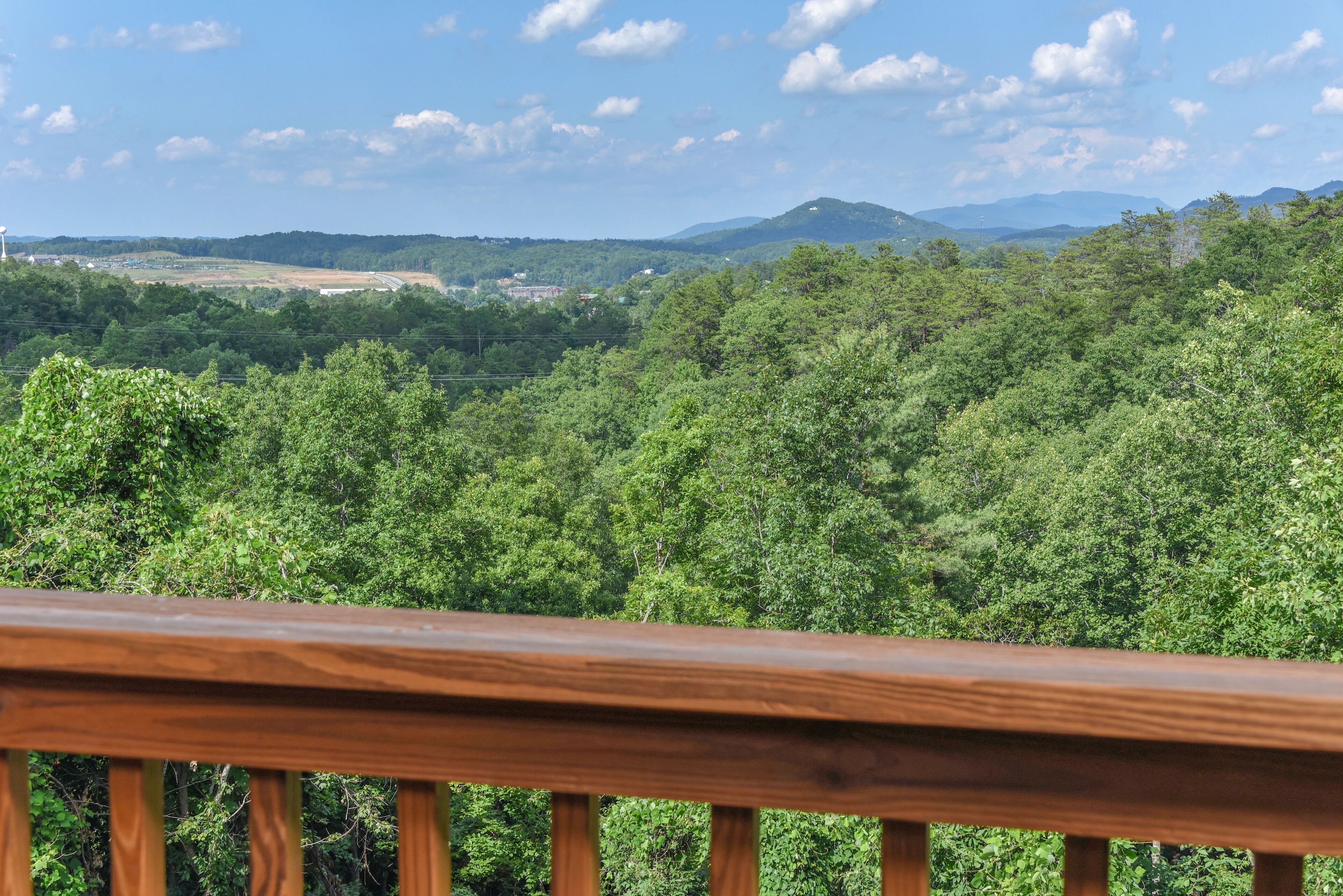 Une vue depuis un balcon en bois donnant sur un paysage verdoyant et luxuriant, avec des montagnes lointaines et un ciel dégagé.
