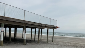 Een houten steiger met een hek van gaas, die naar het strand loopt.