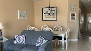 Een woonkamer met een grijze bank, een witte salontafel en een eethoek met een witte tafel en stoelen.