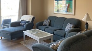 Een woonkamer met een bank, een salontafel, een plafondventilator en een schilderij aan de muur.