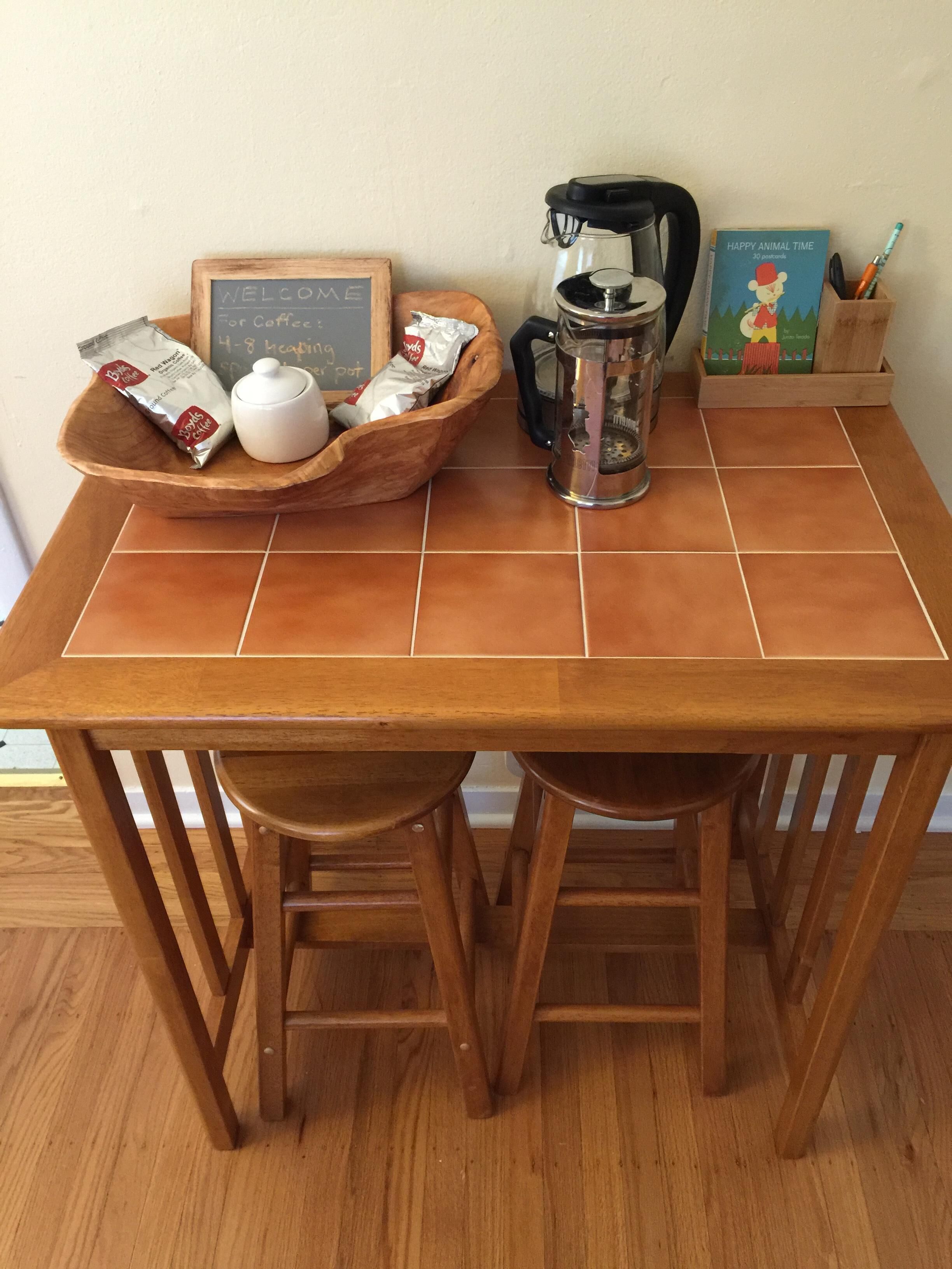 A wooden table with a coffee maker, a teapot, and a tray with coffee packets.