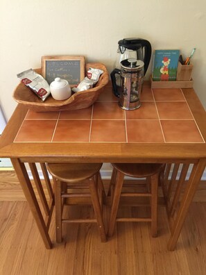 Una mesa de madera con una cafetera, un hervidor y una bandeja con sobres de café.