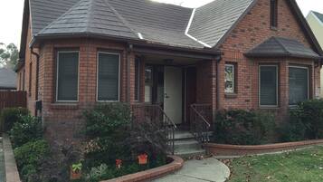 A two-story brick house with a gabled roof, a front porch, and a small front yard with shrubs and a brick border.