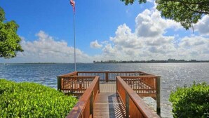 A wooden dock extending into a calm body of water with a flag on a pole, surrounded by lush greenery. - 10/10 EXCEPTIONAL!!! -161 REVIEWS-ANNA MARIA ISLAND-2B/2B-RENOVATED-WELL STOCKED (Bradenton Beach)