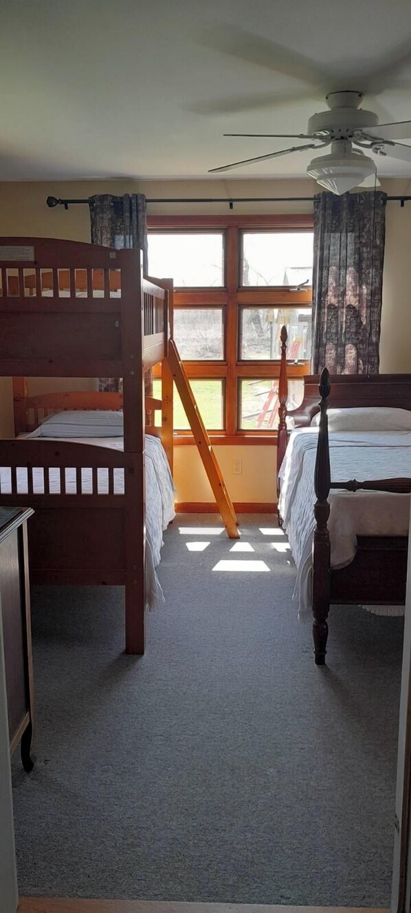 Una habitación con dos literas de madera, un ventilador de techo y una ventana con cortinas.