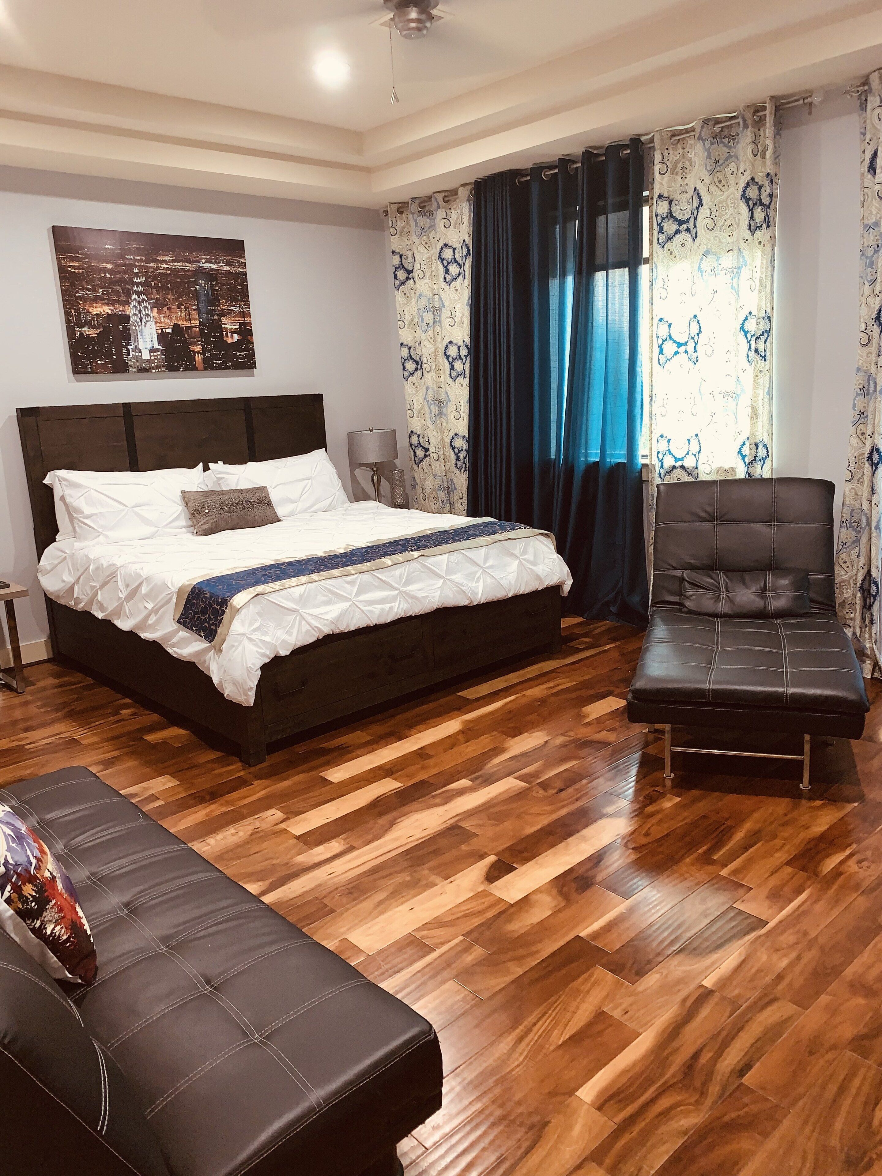 Ein Schlafzimmer mit einem großen Bett, Holzboden, einem Sessel und einem Nachttisch.
