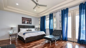 Une chambre à coucher avec un lit, une chaise, un ventilateur de plafond et une fenêtre avec des rideaux.