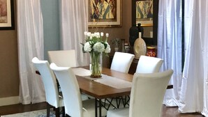 Un coin repas avec une table en bois, des chaises blanches, un vase de fleurs et un lustre.