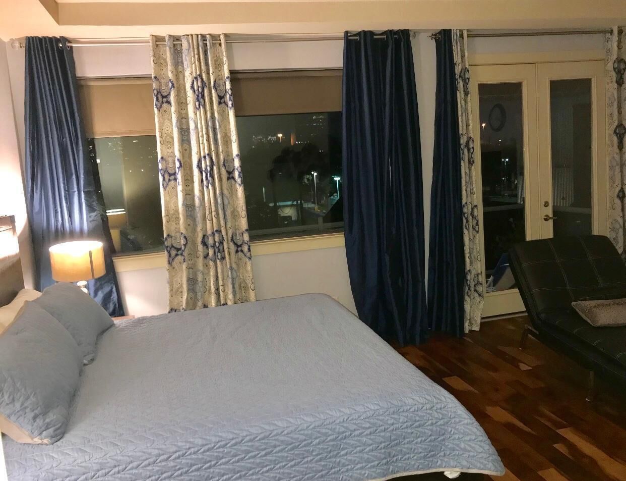 Hotellihuone, jossa on sänky, tuoli, ikkuna verhoilla ja ovi.