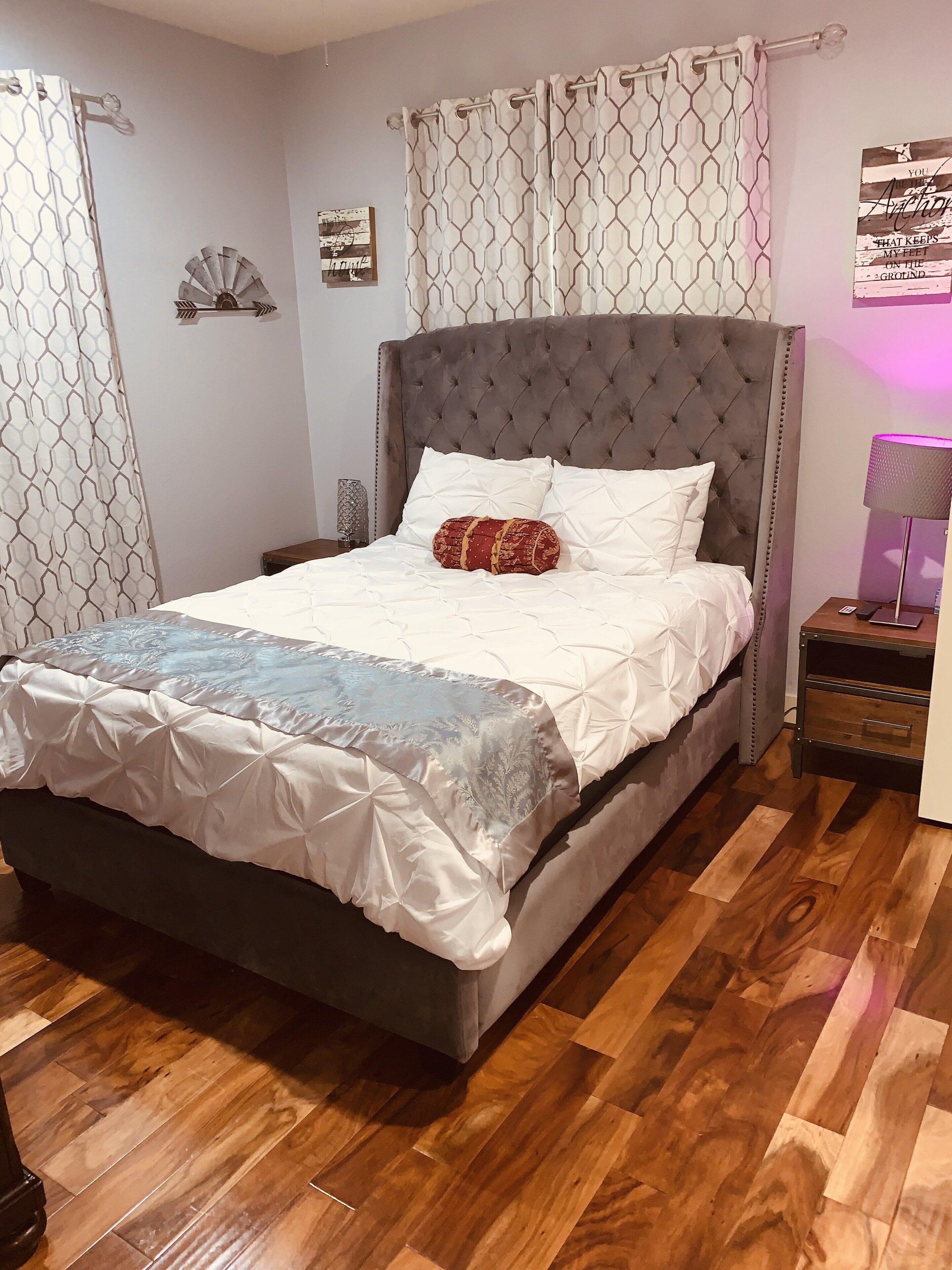 Een net opgemaakt bed met een grijs hoofdeinde, een decoratief kussen en een bedsprei met dessin.