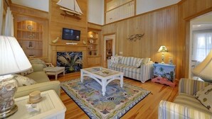 Un salon spacieux avec des boiseries, un ventilateur de plafond, un téléviseur et une grande fenêtre.