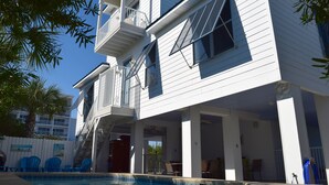 Ein zweistöckiges Haus mit Balkon, Pool und Sitzgelegenheiten im Freien.