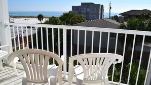 Ein Balkon mit weißen Stühlen mit Blick auf einen Strand und Gebäude.