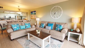 A living room with a sofa, coffee table, and a side table with lamps. There is a large wall clock and a painting on the wall.