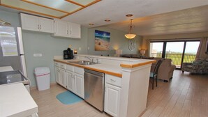 A kitchen with white cabinets, a stainless steel dishwasher, and a wooden countertop. There is a small trash bin and a blue mat on the floor.