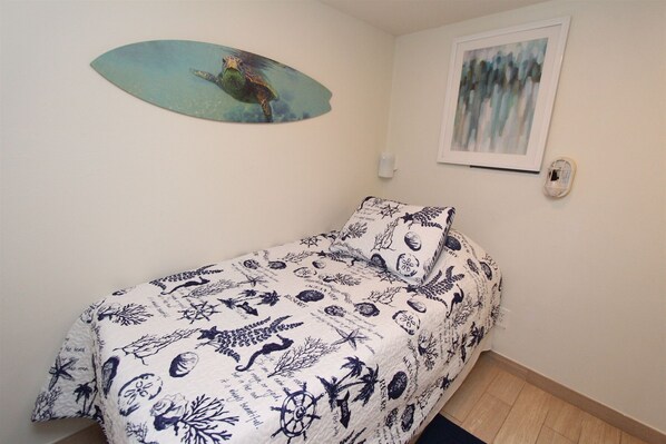 Ein Schlafzimmer mit einem Bett, das mit einer blau-weißen Tagesdecke bezogen ist, einer Wand mit einem gerahmten Gemälde und einer kleinen Wandleuchte.