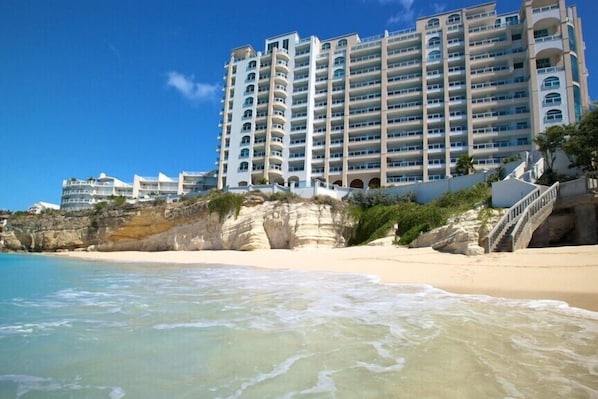 A beachfront hotel with multiple balconies, a sandy beach, and a rocky cliff.