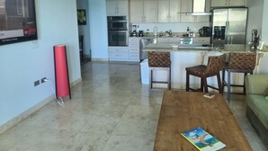 A modern kitchen with white cabinets, a stainless steel refrigerator, and a built-in oven. There is a wooden dining table with a magazine on it. - The Cliff At Cupecoy Beach HEAVEN!!! (Cupecoy)